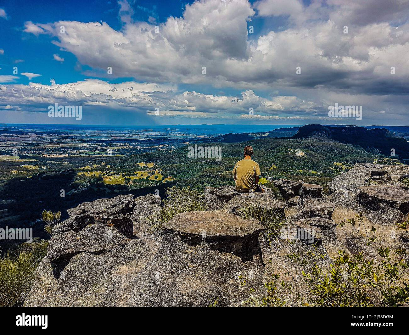 Un jeune homme s'assoit sur un rocher et surplombe le vaste paysage de la vallée de Kangaroo à Broughton Vale, en Nouvelle-Galles du Sud, en Australie Banque D'Images