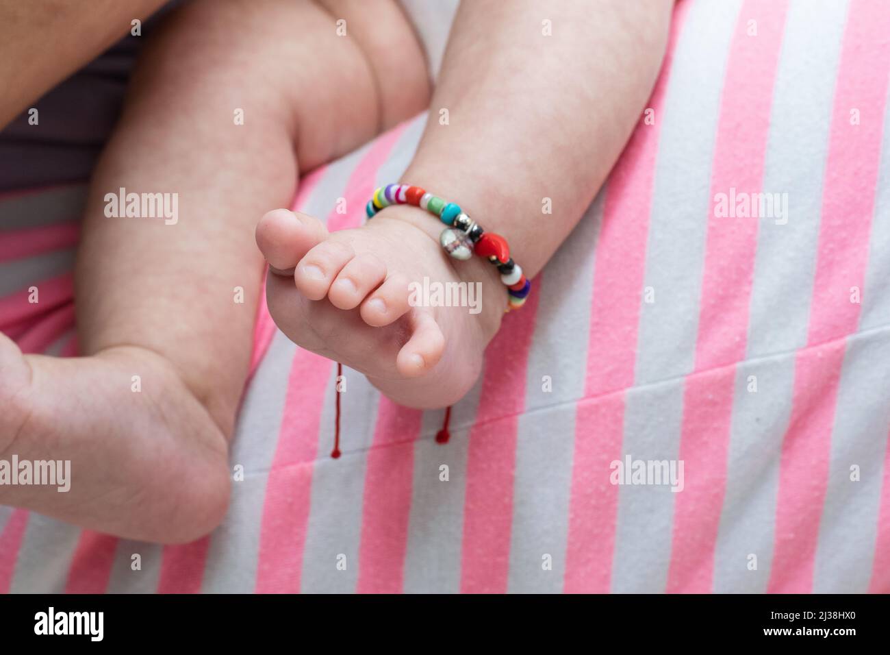 gros plan des pieds d'un bébé porté par sa mère, tout en dormant sur ses jambes. pieds de bébé avec bracelet de cheville, très coloré. Banque D'Images