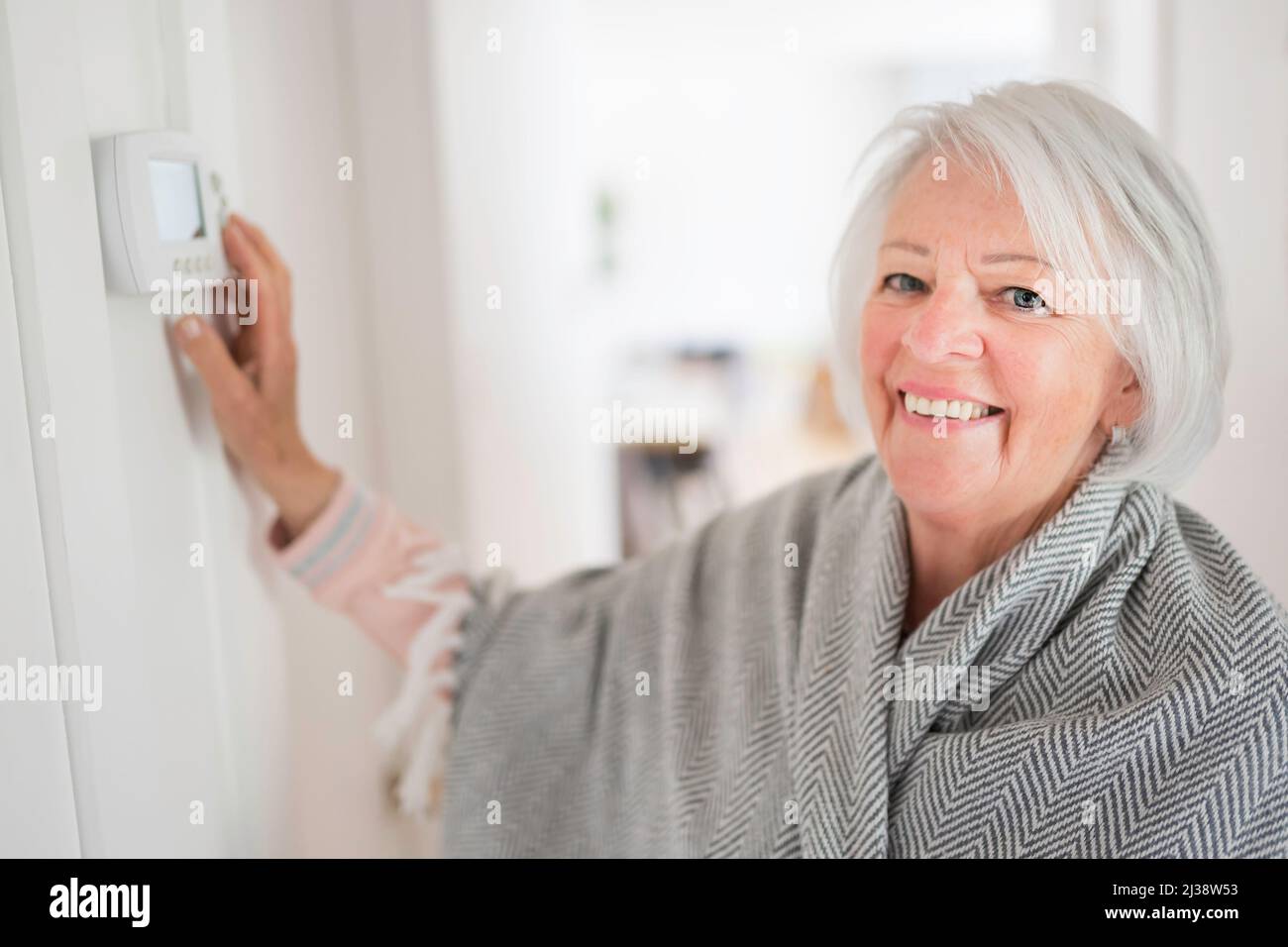 Femme âgée réglant son thermostat à la maison Banque D'Images
