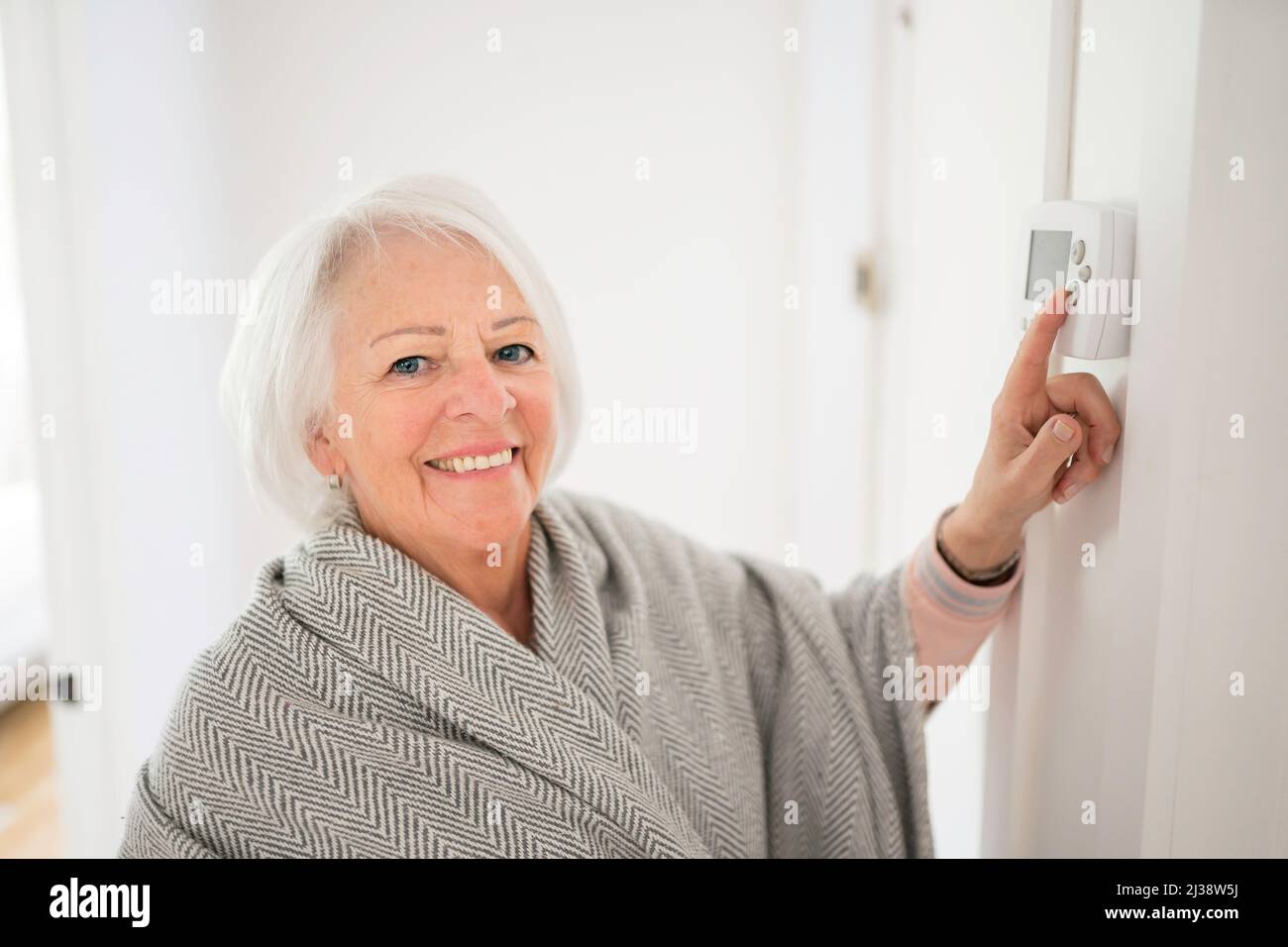 Femme âgée réglant son thermostat à la maison Banque D'Images
