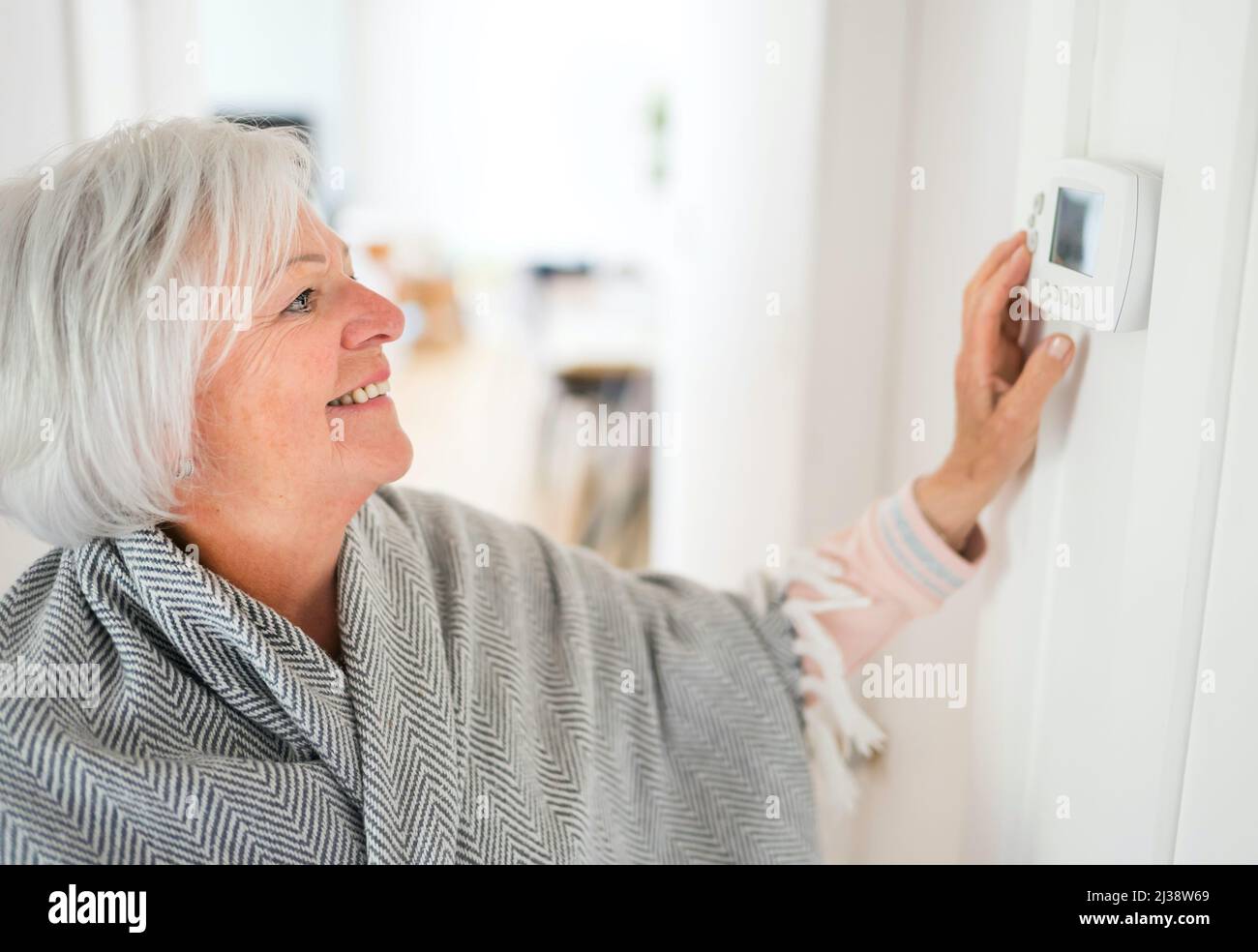 Femme âgée réglant son thermostat à la maison Banque D'Images