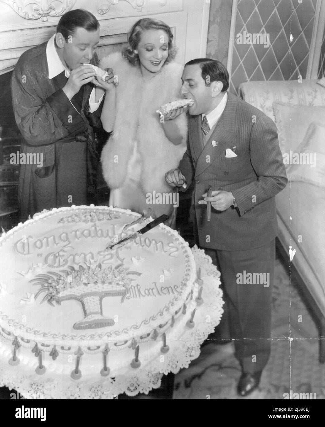 Dietrich Fetes Lubitsch -- eux à la coupe de gâteau. Le gâteau a été décoré avec 25 bougies et a porté l'inscription, 'Félicitations Ernst, Marlene.' L'ensemble de la société de cinéma de plus de 50 personnes a rejoint le parti. Il y a exactement 25 ans, Ernst Lubitsch a commencé à réaliser sa première photo en 1912, à Templehof, une banlieue de Berlin. En l'honneur de cette occasion, Marlene Dietrich a donné une fête pour lui-sur la scène où il dirige et Herbert Marshall dans le 'Angel' de Paramount. 15 novembre 1937. (Photo de C.E. Gatward) Banque D'Images