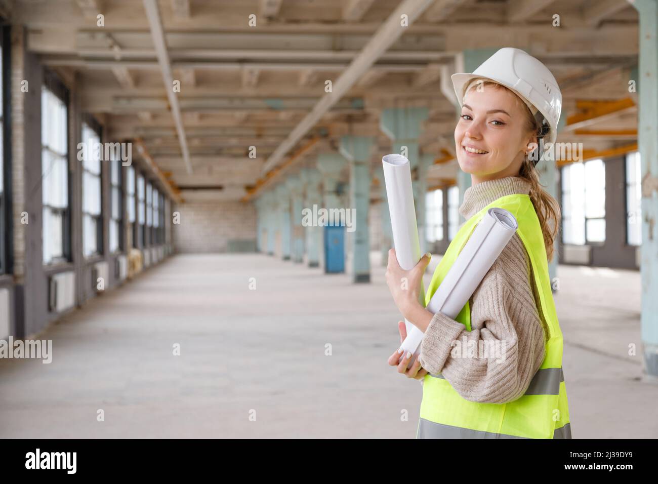 Femme architecte en casque de protection et gilet jaune vérifie le projet de rénovation du bâtiment sur les dessins Banque D'Images