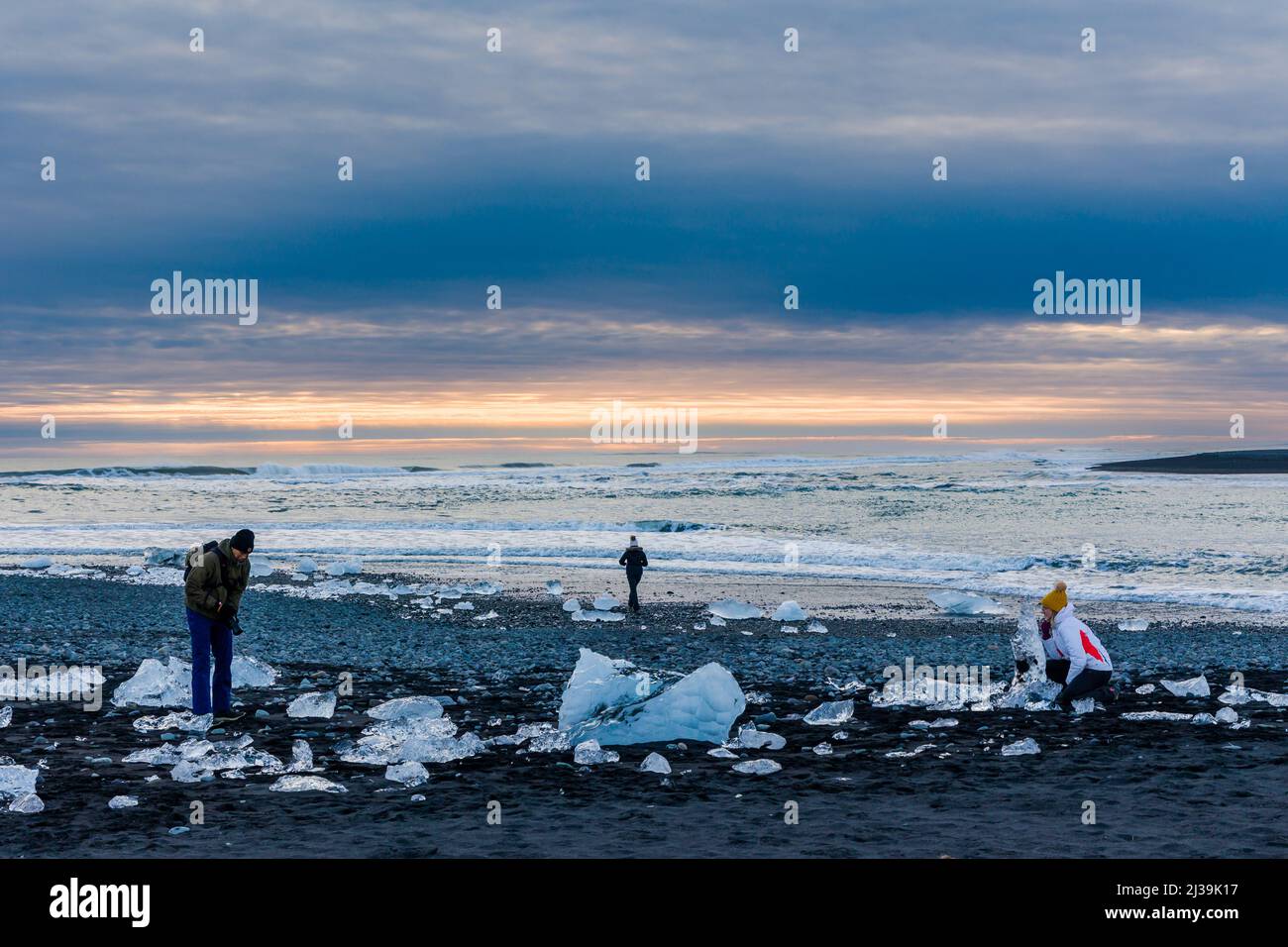 JOKULSARLON,ISLANDE - NOVEMBRE 18 2021: Touristes examinant des icebergs et des cristaux sur la plage de sable noir à Jokulsarlon, Islande Banque D'Images