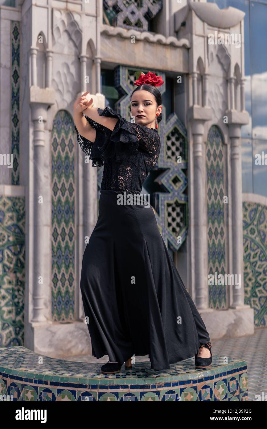 la jeune danseuse espagnole de flamenco vêtue de noir avec une rose rouge dans ses cheveux pose sur une plate-forme carrelée avec une décoration arabe Banque D'Images