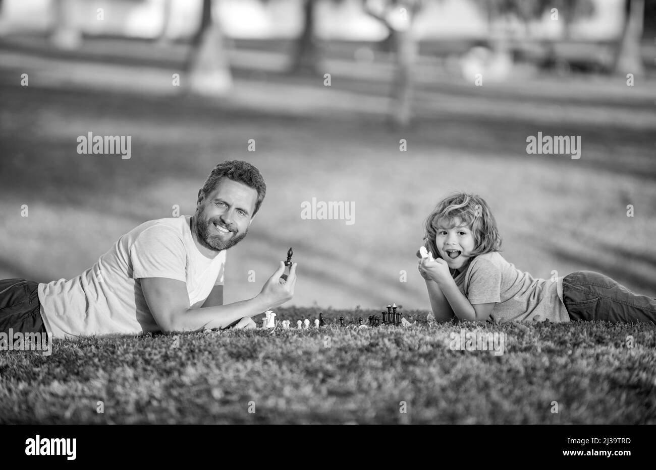 famille heureuse de père homme et fils enfant jouant aux échecs sur l'herbe verte dans le parc extérieur, paternité Banque D'Images
