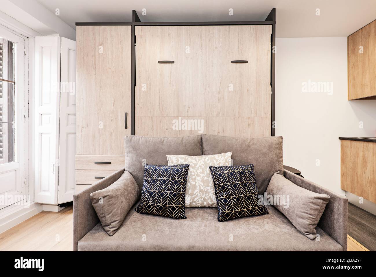 canapé-lit en tissu gris avec coussins bleus et blancs, balcon avec volets en bois et armoire intégrée dans le studio de location de vacances Banque D'Images