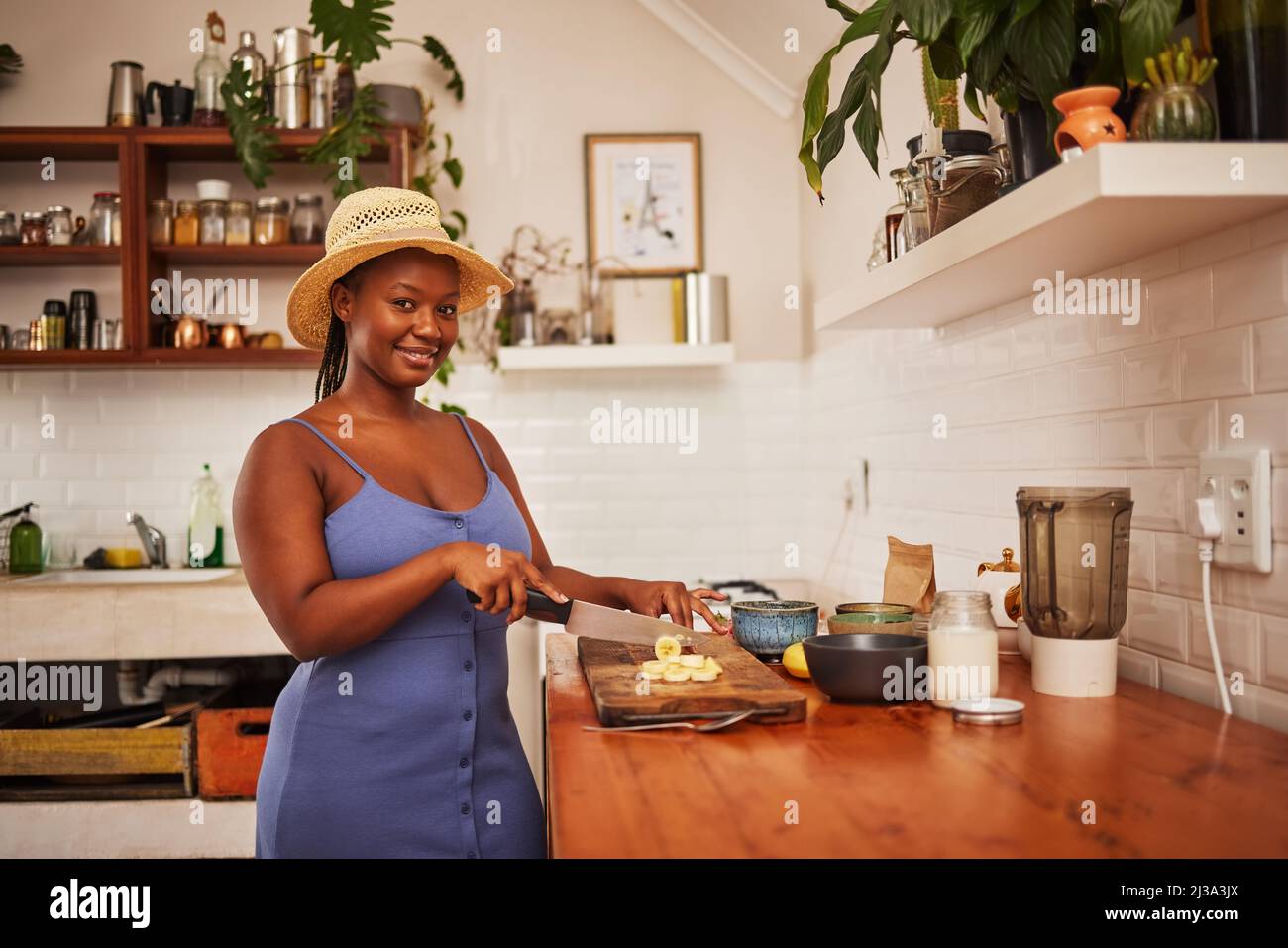 Dieu sait que j'ai le temps de donner. Portrait d'une jeune belle femme portant un chapeau de soleil tout en coupant des fruits dans la cuisine à la maison. Banque D'Images