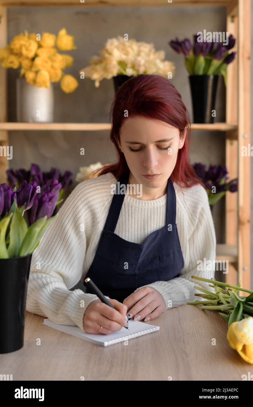 Portrait d'une dame du caucase dans un tablier. Une femme propriétaire d'entreprise de fleurs a écrit une commande pour un bouquet de fleurs dans un carnet. Fleur européenne Banque D'Images