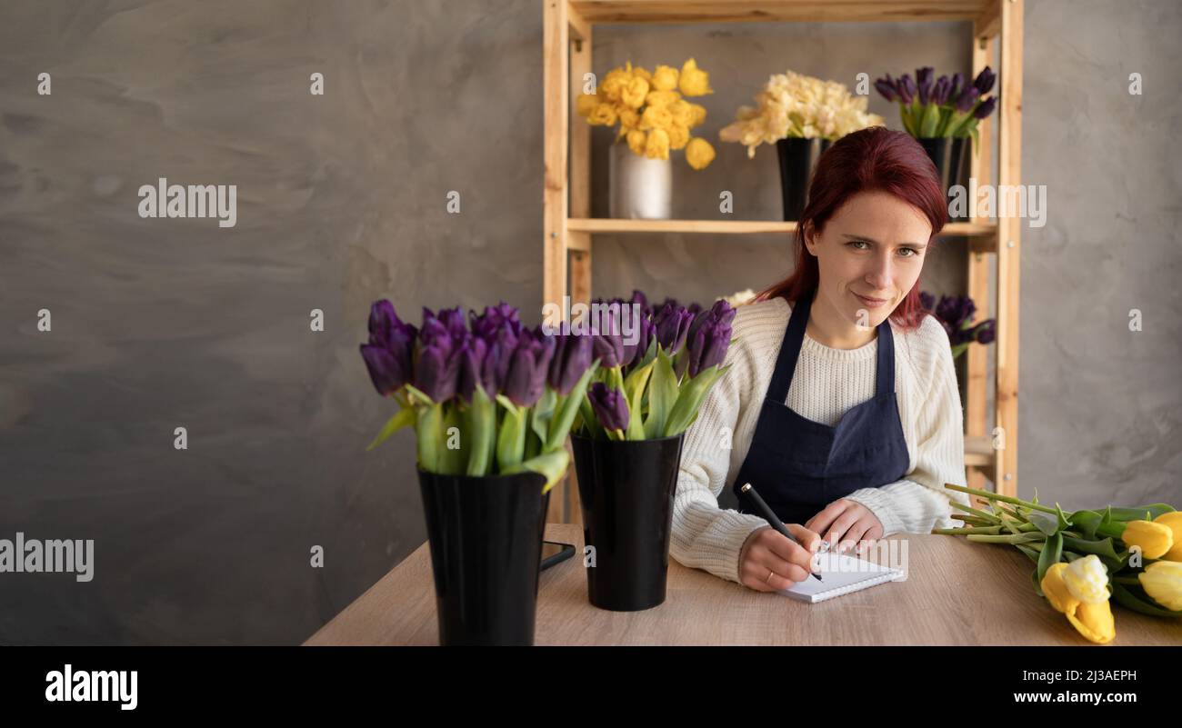 Concept de fleuriste européen. Une fleuriste est assise à une table tenant un stylo dans ses mains et faisant des demandes pour la livraison des plantes et Banque D'Images