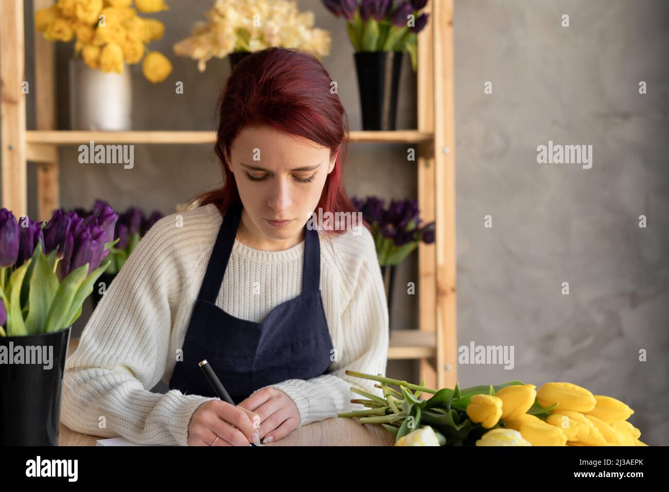 Une femme propriétaire d'entreprise de fleurs a écrit une commande pour un bouquet de fleurs dans un carnet. Concept de fleuriste européen. Banque D'Images