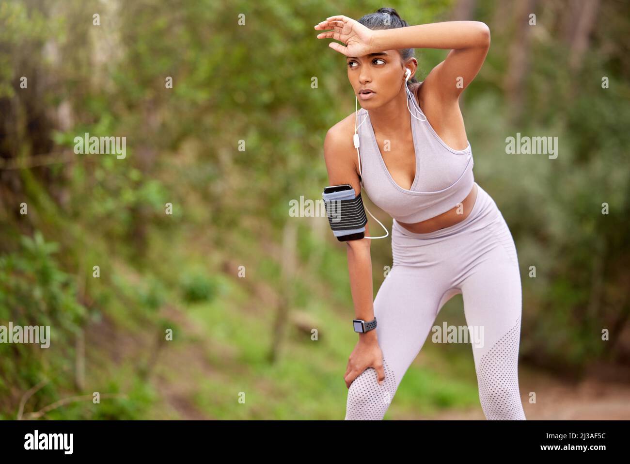 Il devient toujours dur à la fin. Photo d'une jeune femme prenant une pause tout en faisant du jogging dans la forêt. Banque D'Images