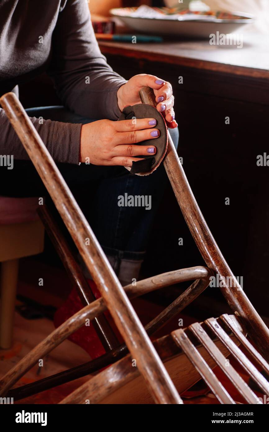 Gros plan de la surface de ponçage de lady assis de tabouret vieilli nécessitant une rénovation avec l'aide de papier de verre dans l'atelier à la maison. Pratiques durables. Réutilisation de Banque D'Images