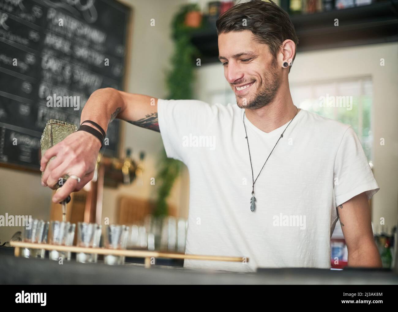 Les tireurs sont une entrée instantanée de la fête. Photo d'un jeune barman heureux qui verse des photos derrière le bar. Banque D'Images