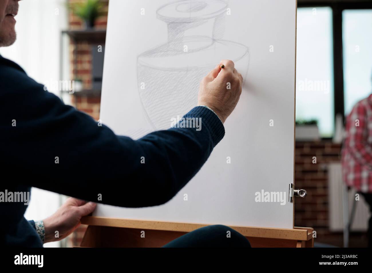 Gros plan du peintre homme senior dessin vase croquis sur toile blanche à l'aide d'un crayon d'illustration pendant la classe d'art dans l'atelier créatif. Artiste esquissant une œuvre développant une technique graphique Banque D'Images