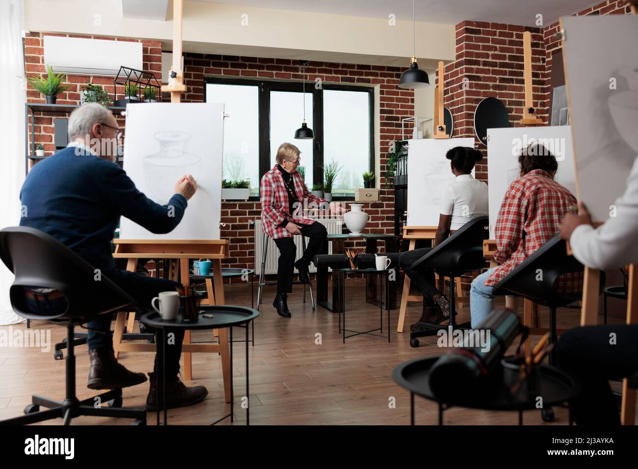 Professeur principal expliquant la technique de dessin aux étudiants multiethniques pendant l'atelier de création. Diverses équipes apprennent à dessiner un modèle sur toile à l'aide d'un crayon graphique. Résolutions du nouvel an Banque D'Images