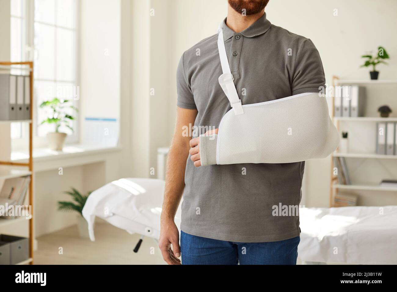 Un inconnu portant un bandage pour harnais de bras sur un bras cassé est debout dans un bureau médical. Banque D'Images