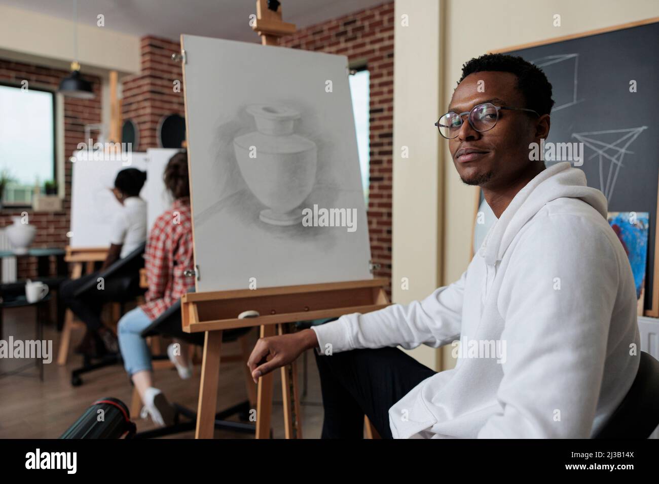 Portrait d'un étudiant afro-américain souriant qui s'adresse à une classe d'art et qui développe une nouvelle compétence artistique pour la croissance personnelle. Divers modèles de vase de dessin d'équipe travaillant à la technique graphique. Concept créatif Banque D'Images