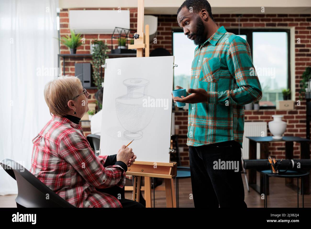 Jeune peintre enseignant expliquant l'illustration du croquis à la femme senior travaillant ensemble au dessin graphique dans le studio de créativité. Divers équipe dessin vase modèle sur toile apprentissage de nouvelles compétences artistiques Banque D'Images