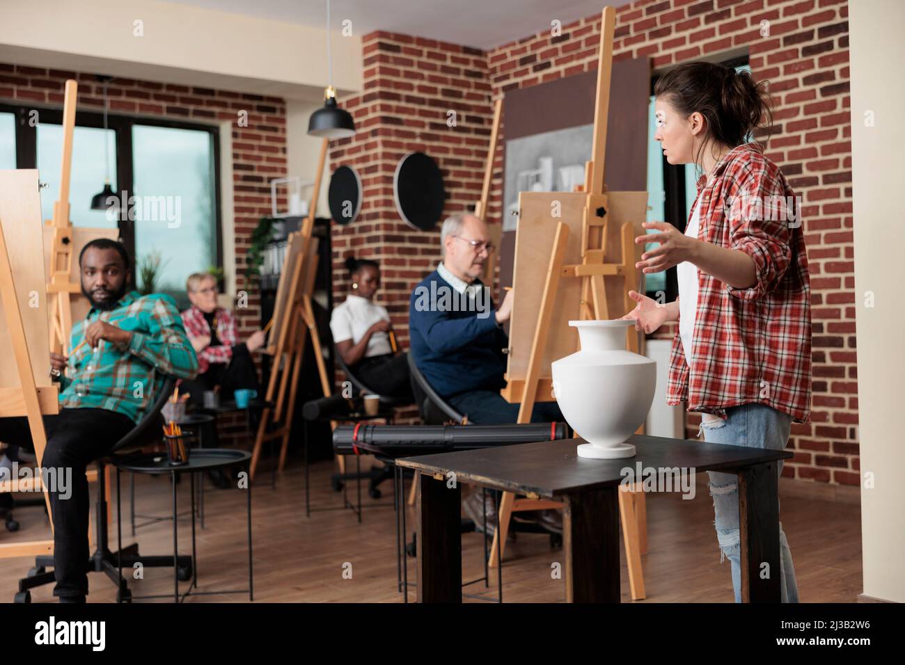 Professeur de peintre supervisant l'homme senior tout en dessinant le modèle de vase sur toile travaillant à la technique d'illustration dans le studio de créativité. Une équipe diversifiée qui s'adresse à des cours d'art et développe des compétences artistiques Banque D'Images