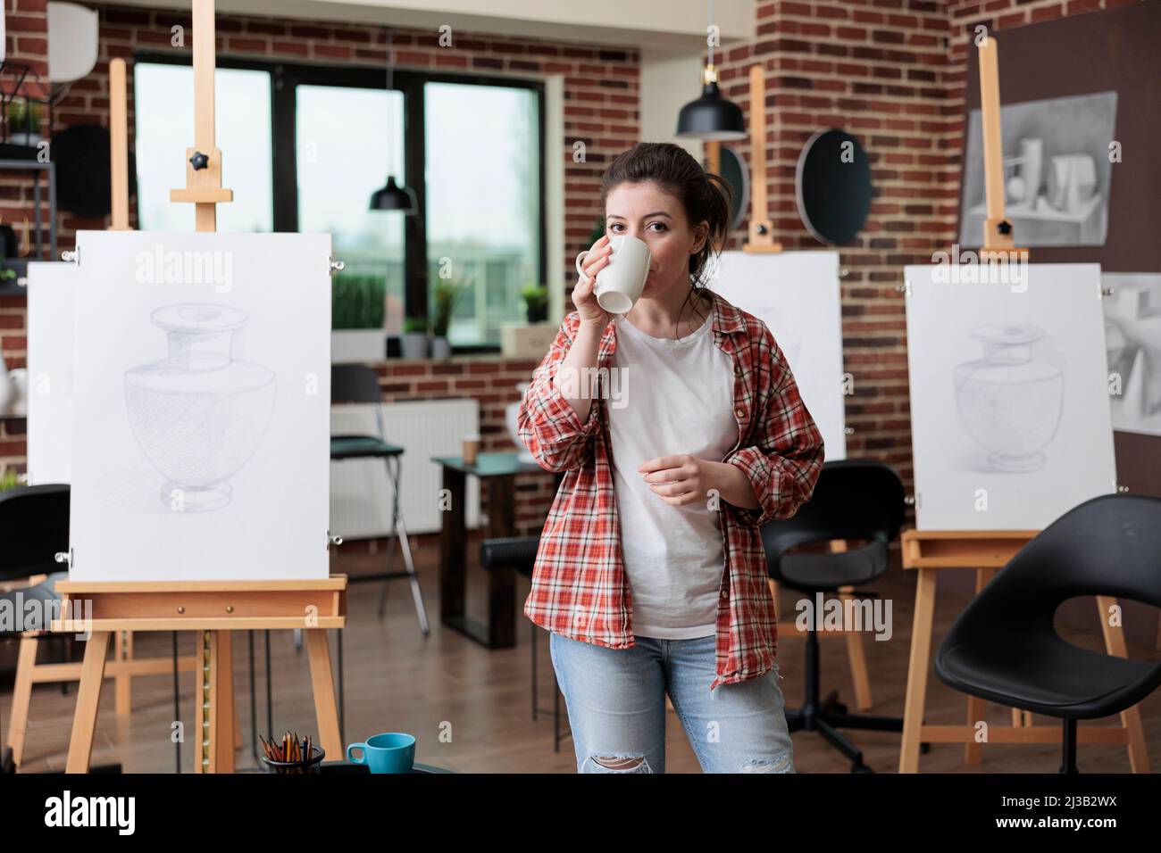 Portrait d'un professeur d'art debout dans un lieu de travail créatif boire du café avant de commencer à travailler à l'illustration du croquis à l'aide d'un crayon graphique. Jeune artiste développant des compétences artistiques pour la croissance personnelle Banque D'Images