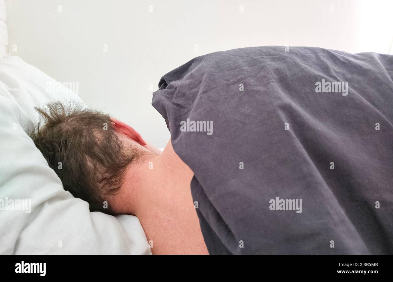 Homme dormant dans un lit sous une couverture le matin. Vue arrière. Banque D'Images