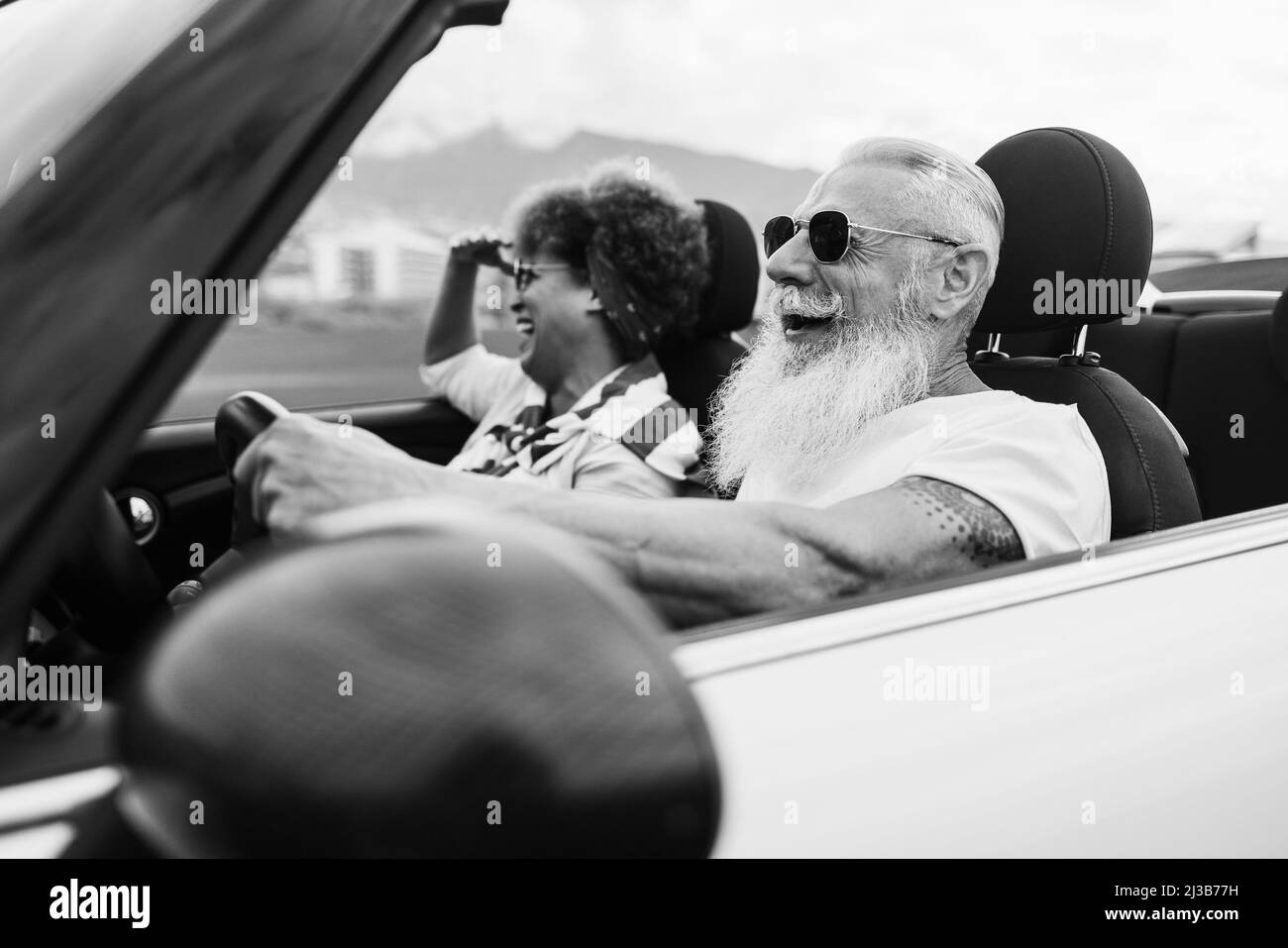 Joyeux couple senior s'amusant en voiture convertible pendant les vacances d'été - Focus sur le visage de l'homme - montage noir et blanc Banque D'Images Joyeux couple senior s'amusant en voiture convertible pendant les vacances d'été - Focus sur le visage de l'homme - montage noir et blanc Banque D'Images