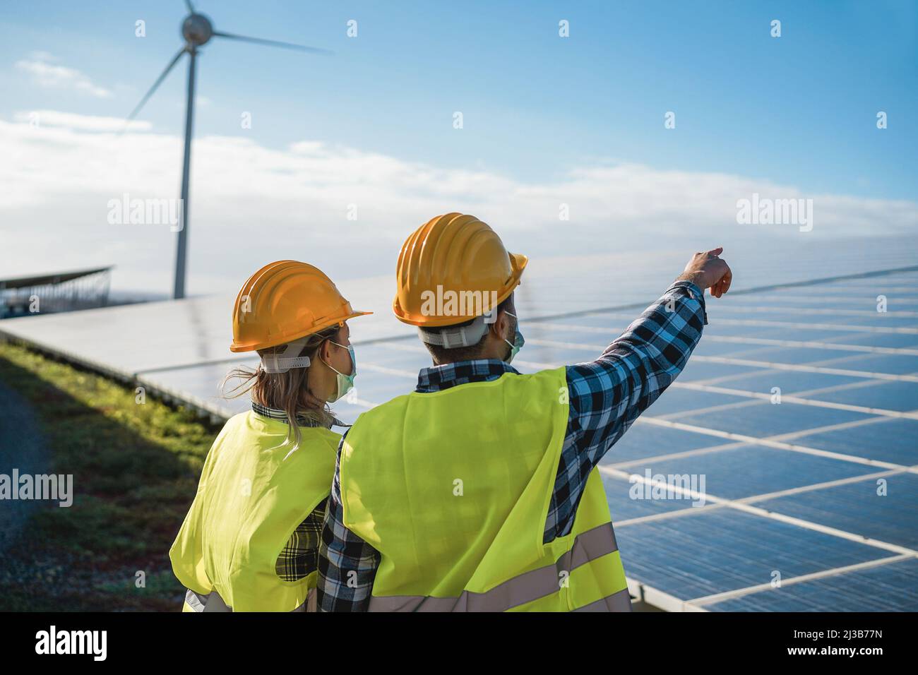 Les personnes travaillant pour des panneaux solaires et des éoliennes dans une ferme d'énergie renouvelable portant des masques de sécurité - Focus sur le casque femme Banque D'Images