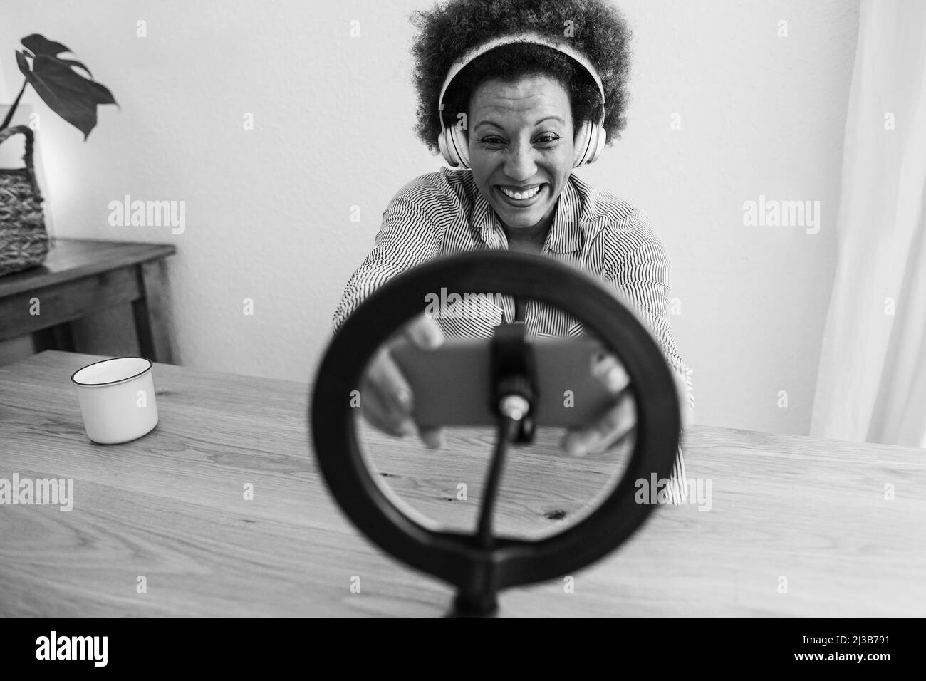 Bonne femme africaine senior ayant plaisir à diffuser en ligne avec le téléphone mobile à la maison - Focus sur le visage - montage noir et blanc Banque D'Images
