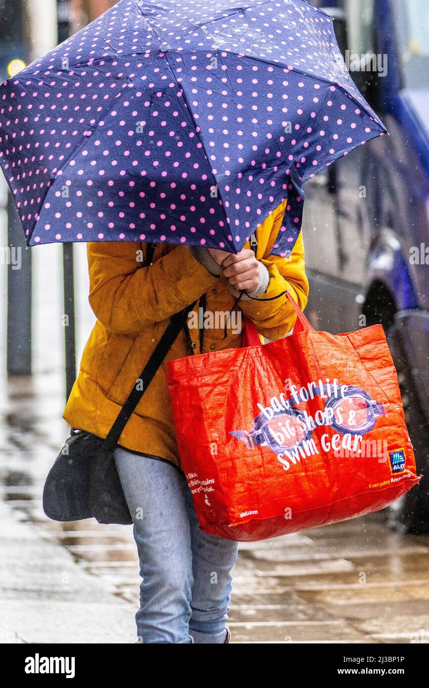 Femme tenant un sac d'équipement rouge « Swim Gear bag for Life » lors d'un jour de pluie à Preston, dans le Lancashire. Météo au Royaume-Uni 07 avril 2022. Vents forts et forts inconvénients à Preston à mesure que les températures chutent à 7c. Les clients qui s'étouffent lorsque la pluie battante et les vents violents étouffent les esprits de la rue. Très venteux avec des douches d'avril tout au long de la journée. Crédit : MediaWorldImages/AlamyLiveNews Banque D'Images