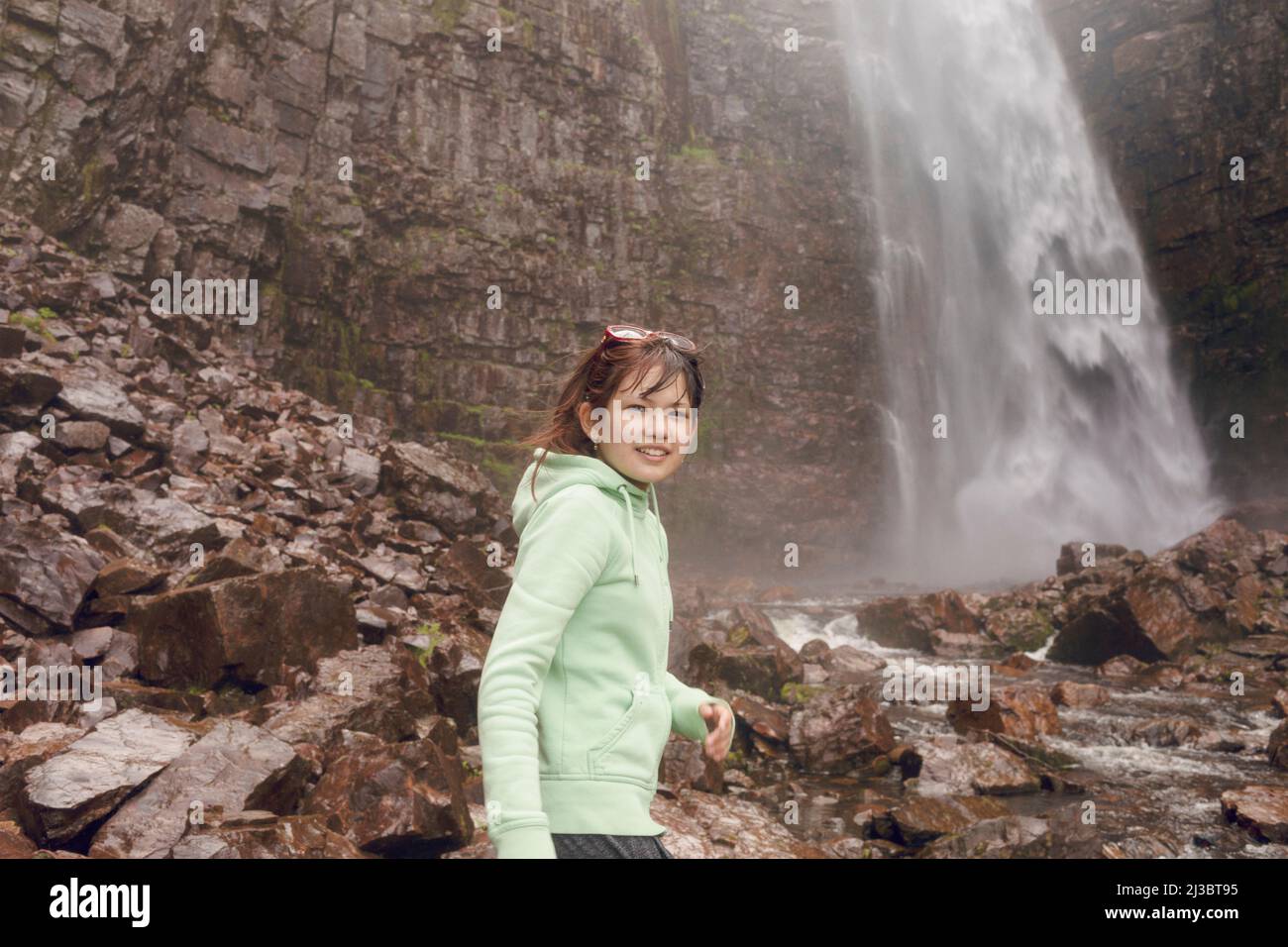 Fille souriante debout devant la cascade Banque D'Images