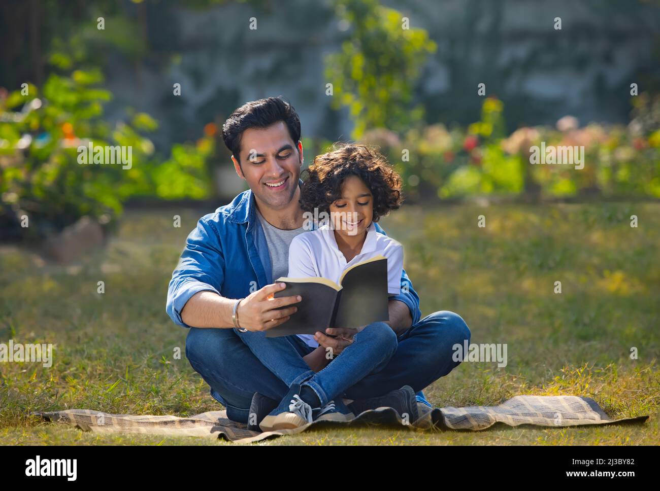 Enfant garçon lisant le livre tout en étant assis sur les genoux de son père dans le parc Banque D'Images