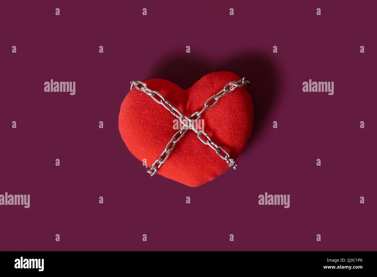 Dépendance d'amour. Un coeur jouet enroulé par une chaîne sur un fond coloré Banque D'Images