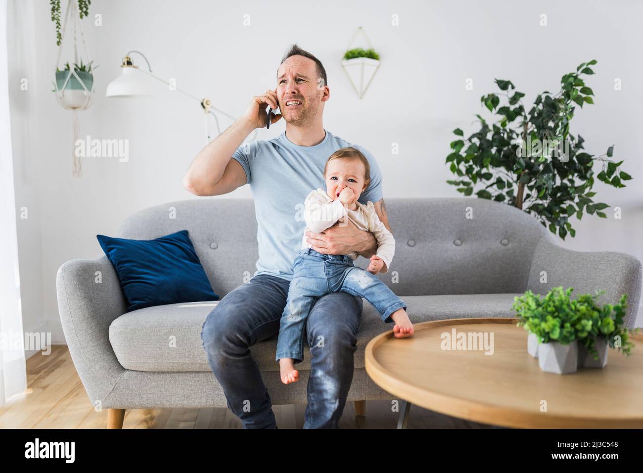 Homme tenant un bébé hurlant le père appeler l'aide au téléphone Banque D'Images