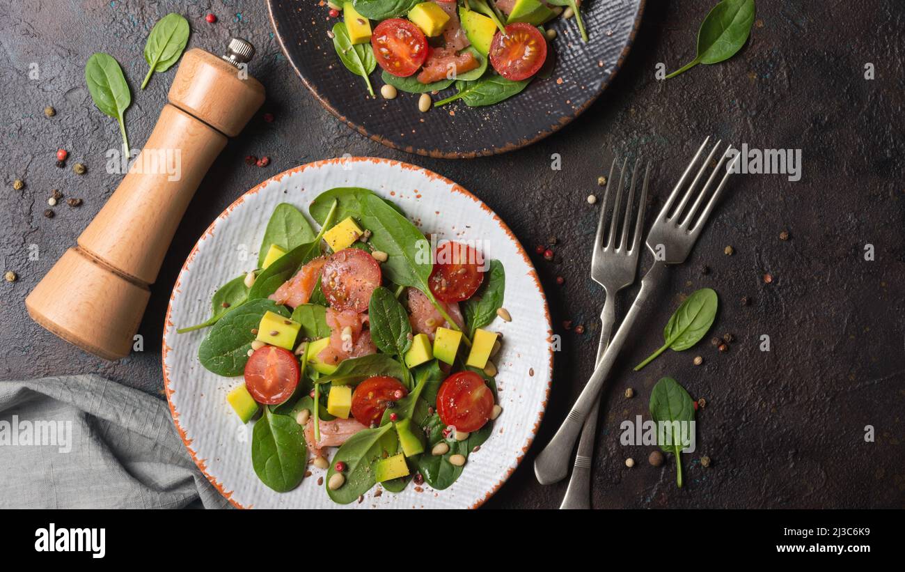 Vue de dessus de la nourriture saine. Salade de jeunes feuilles d'épinards frais, tomates cerises, tranches d'avocat et saumon rouge salé sur fond de béton foncé Banque D'Images