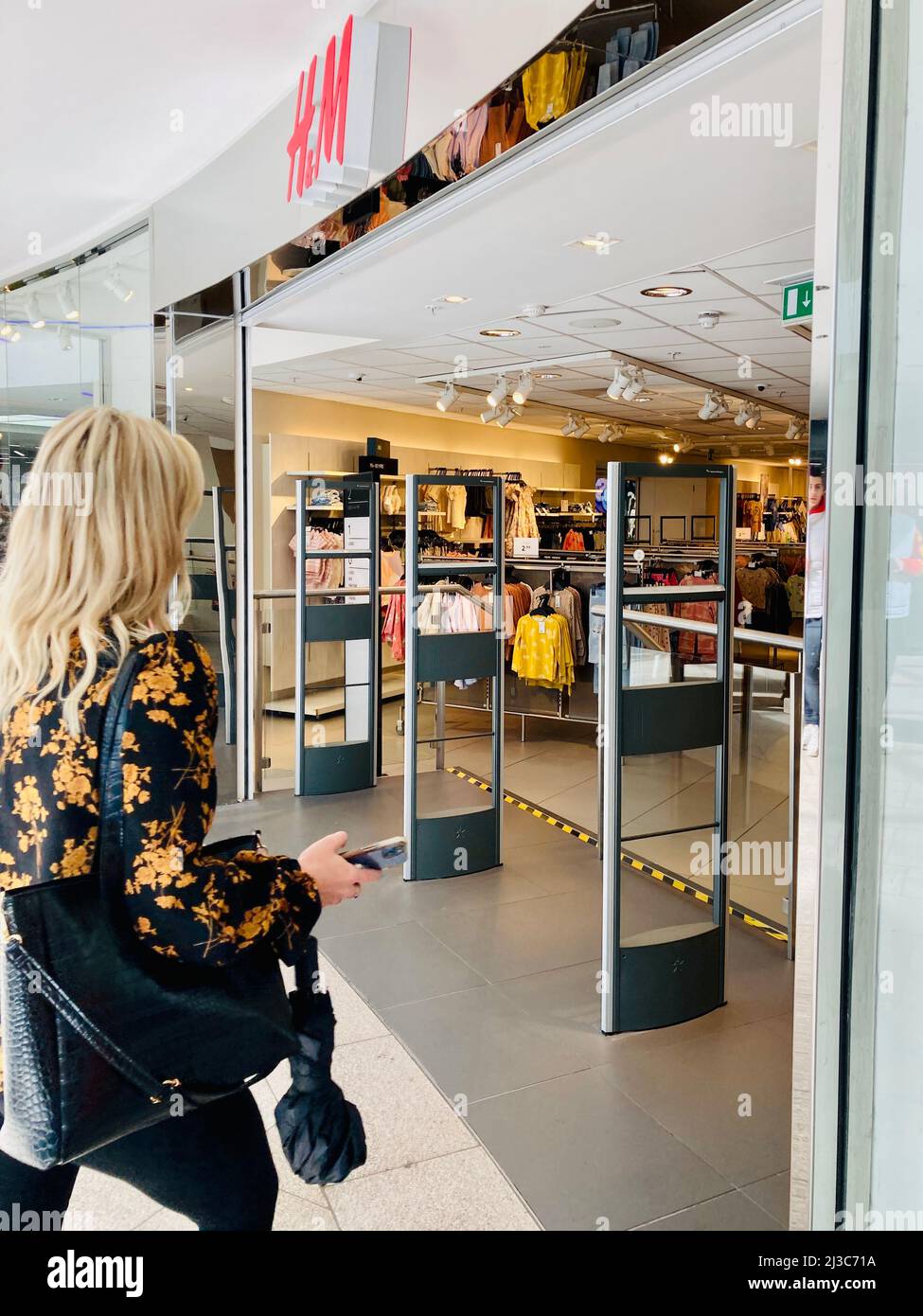 Une femme blonde traversant l entree de la boutique de mode H M High Street dans le centre commercial Leeds Trinity Royaume Uni Photo Stock Alamy