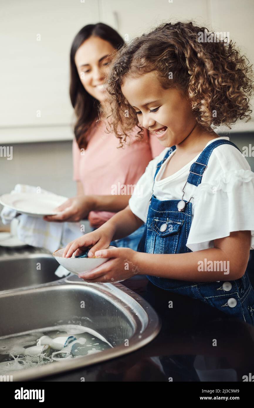 Les corvées font partie de la croissance. Photo d'une adorable jeune fille debout et aidant sa mère avec les plats dans la cuisine à la maison. Banque D'Images
