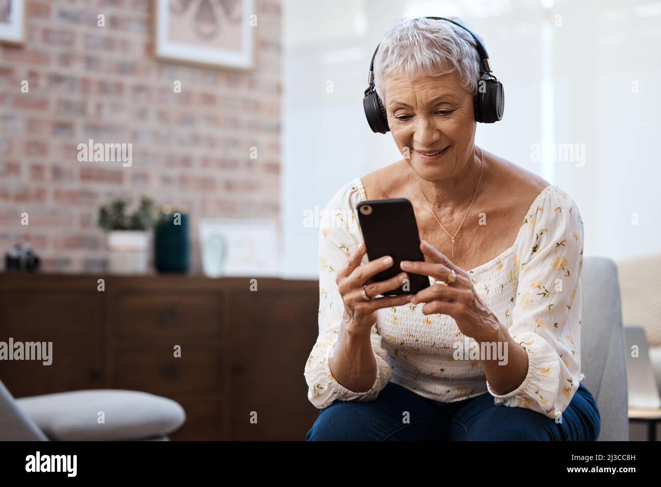 Une nouvelle façon d'écouter de vieilles chansons. Photo d'une femme âgée utilisant un smartphone et un casque sur le canapé à la maison. Banque D'Images