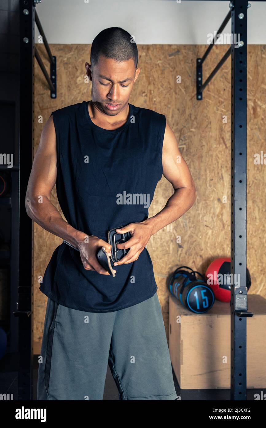 Un sportif afro-américain sérieux se portant sur des vêtements de sport qui  serrent la ceinture d'haltérophilie tout en se tenant dans une salle de gym  légère avec un équipement spécial pendant l'haltérophilie