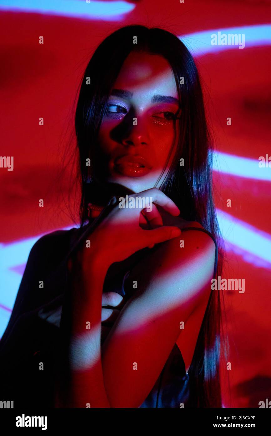 Brunette sérieuse en vêtements de nuit noirs en studio avec éclairage rouge et blanc lumineux provenant du projecteur, en toute confiance Banque D'Images