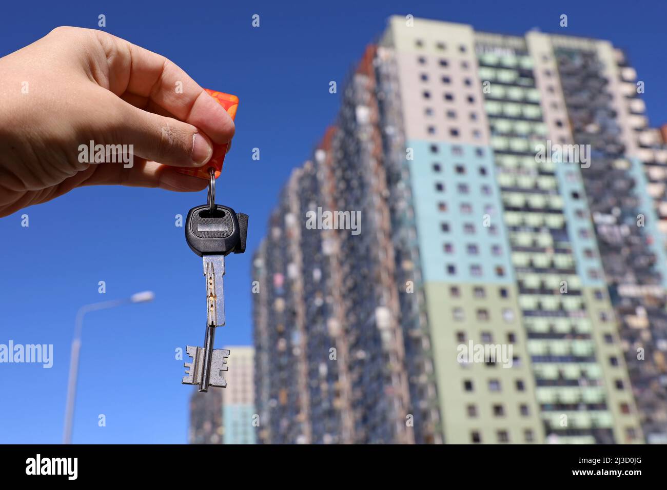 Les clés de la maison dans la main masculine sur fond de nouveaux bâtiments. Agent immobilier, déménagement ou location de biens Banque D'Images