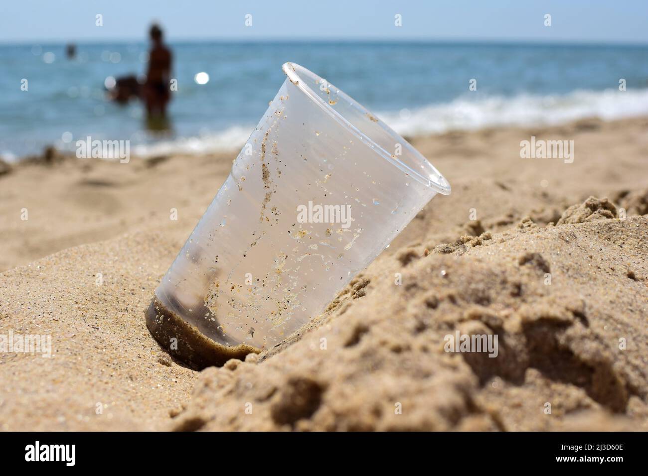 Sur le rivage sablonneux de la plage de la mer se trouve un verre sale en plastique de près. L'arrière-plan est très flou Banque D'Images