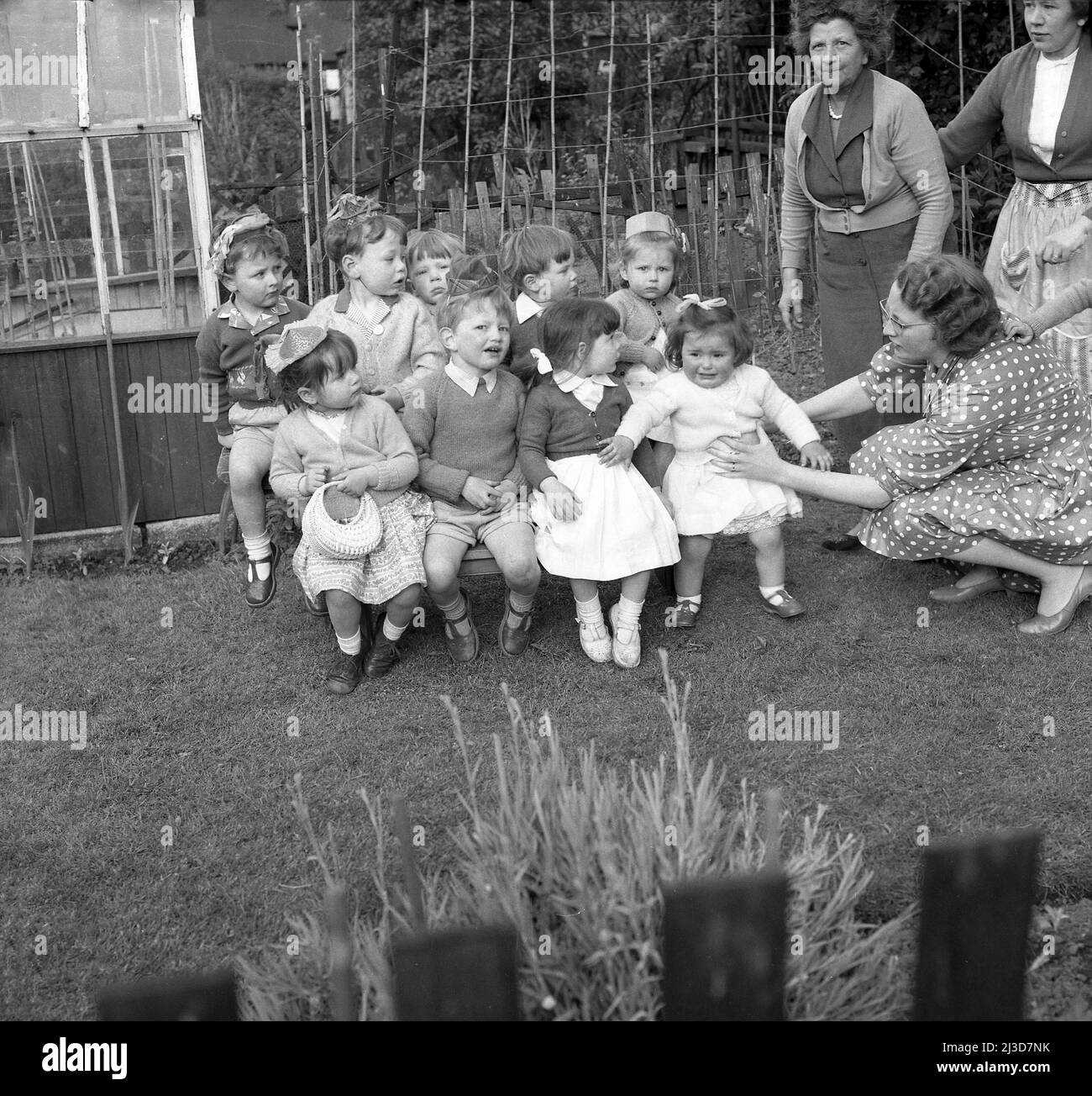 1961, hisotrical, une fête d'anniversaire de trois ans... à l'extérieur dans un jardin, une mère tente de faire s'asseoir sa petite fille impatiente avec les autres enfants pour une photo, Stockport, Manchester, Angleterre, Royaume-Uni. Banque D'Images