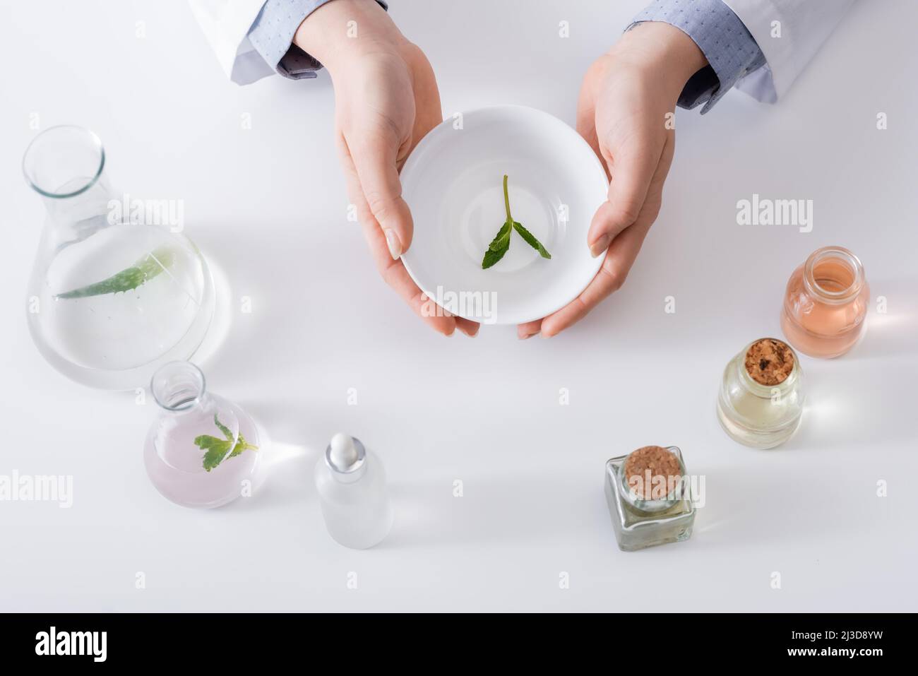 vue de dessus de l'assistant de laboratoire tenant le bol avec des feuilles de menthe près des flacons et des bouteilles Banque D'Images