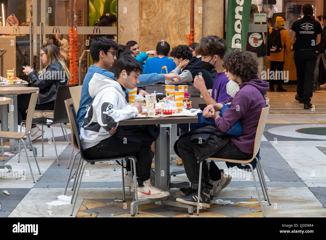 Naples, Italie - le 25 mars 2022 : groupe de jeunes adolescents assis à une table McDonald's en train de manger de la nourriture dans des paquets de papier. Banque D'Images