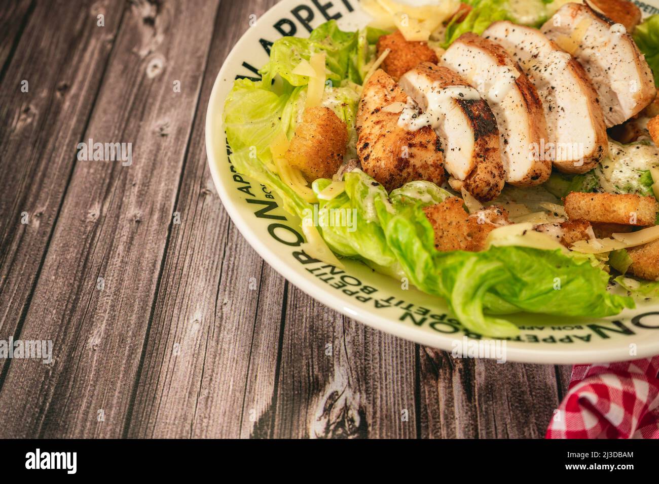 Salade César avec poitrine de poulet finement tranchées et aïoli traditionnel sur une assiette qui dit bon appétit sur une table rustique. Vue en hauteur. Banque D'Images