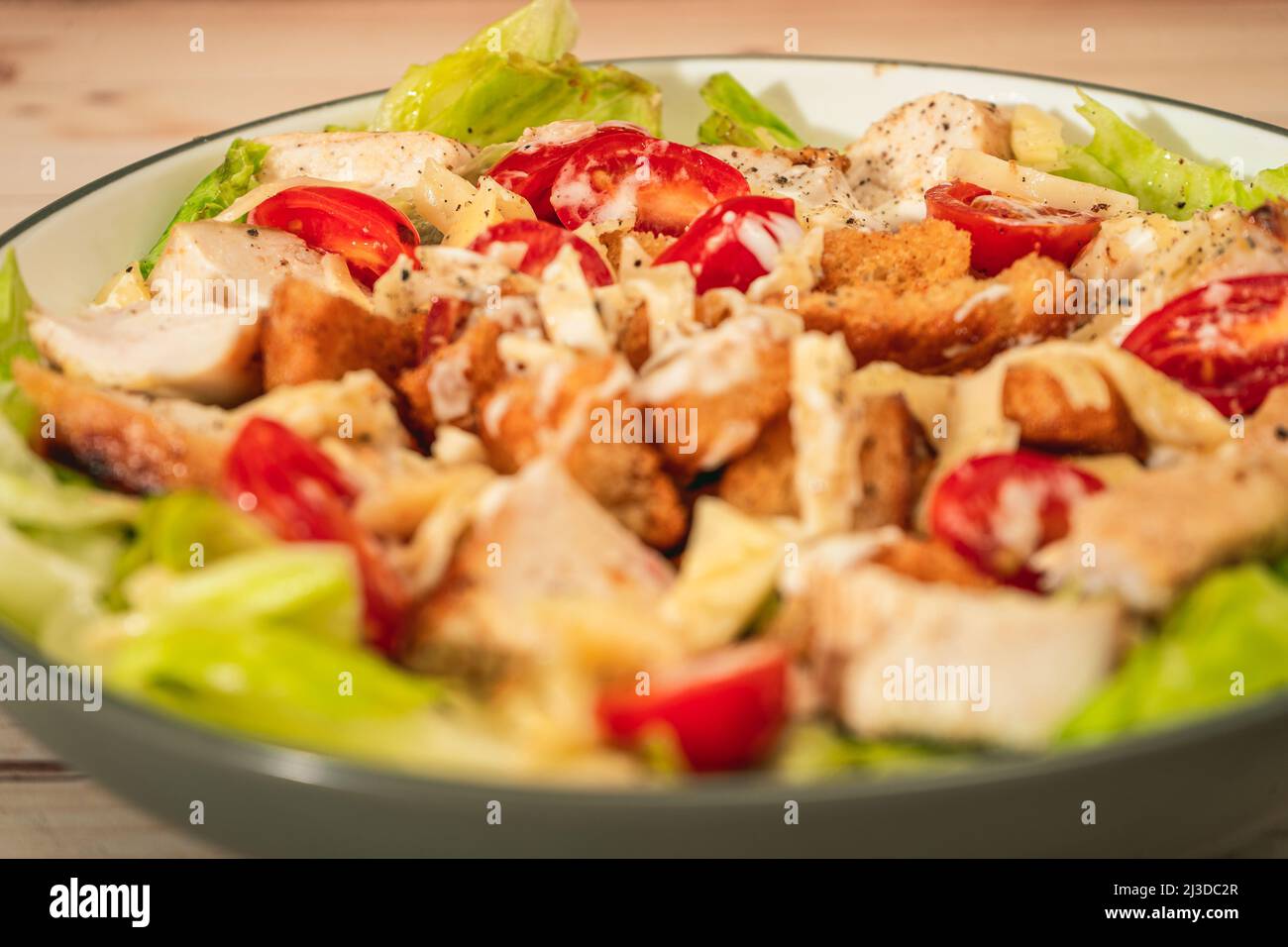 Variante de salade César avec de petites bouchées de poulet, de tomates cerises et une sauce aioli gastronomique dans un petit bol sur une table rustique. Vue en hauteur. Fermer-u Banque D'Images