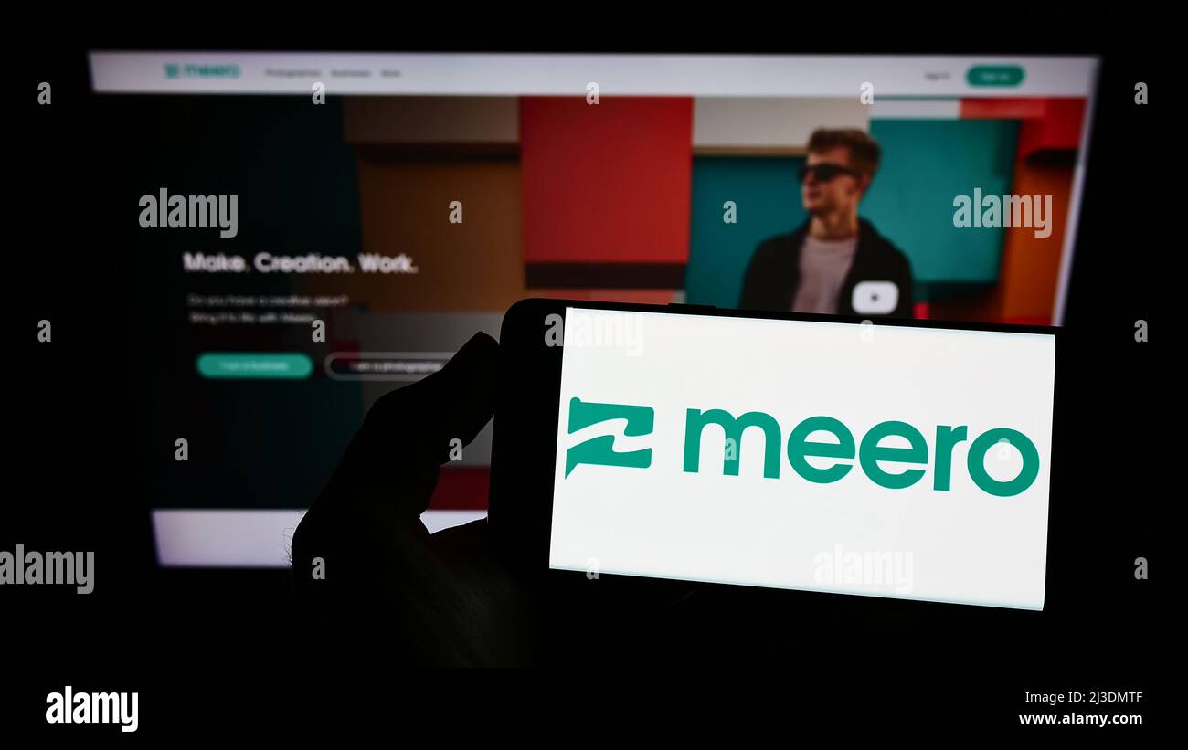 Personne tenant un smartphone avec le logo de la société de photographie française Meero à l'écran devant le site. Mise au point sur l'affichage du téléphone. Banque D'Images
