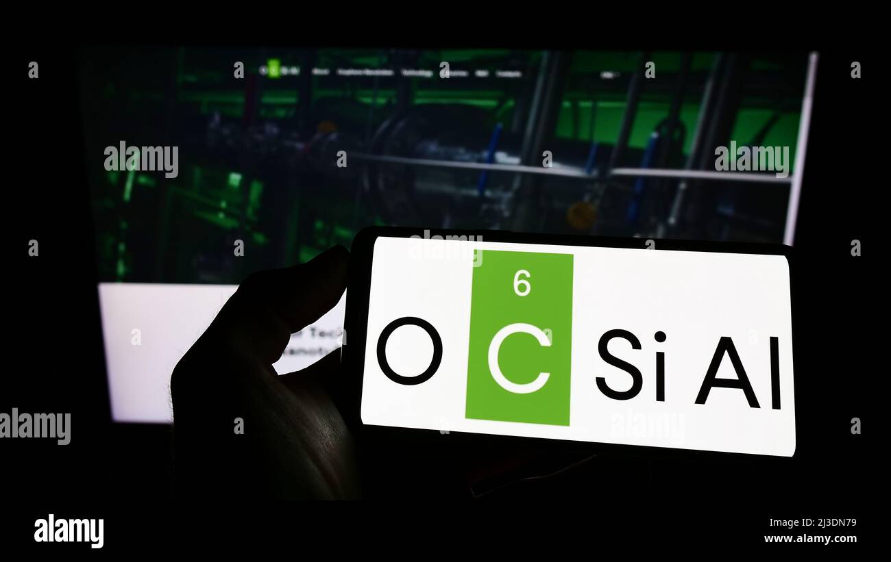 Personne tenant un téléphone portable avec le logo de la société luxembourgeoise OCSiAl à l'écran en face de la page web d'affaires. Mise au point sur l'affichage du téléphone. Banque D'Images
