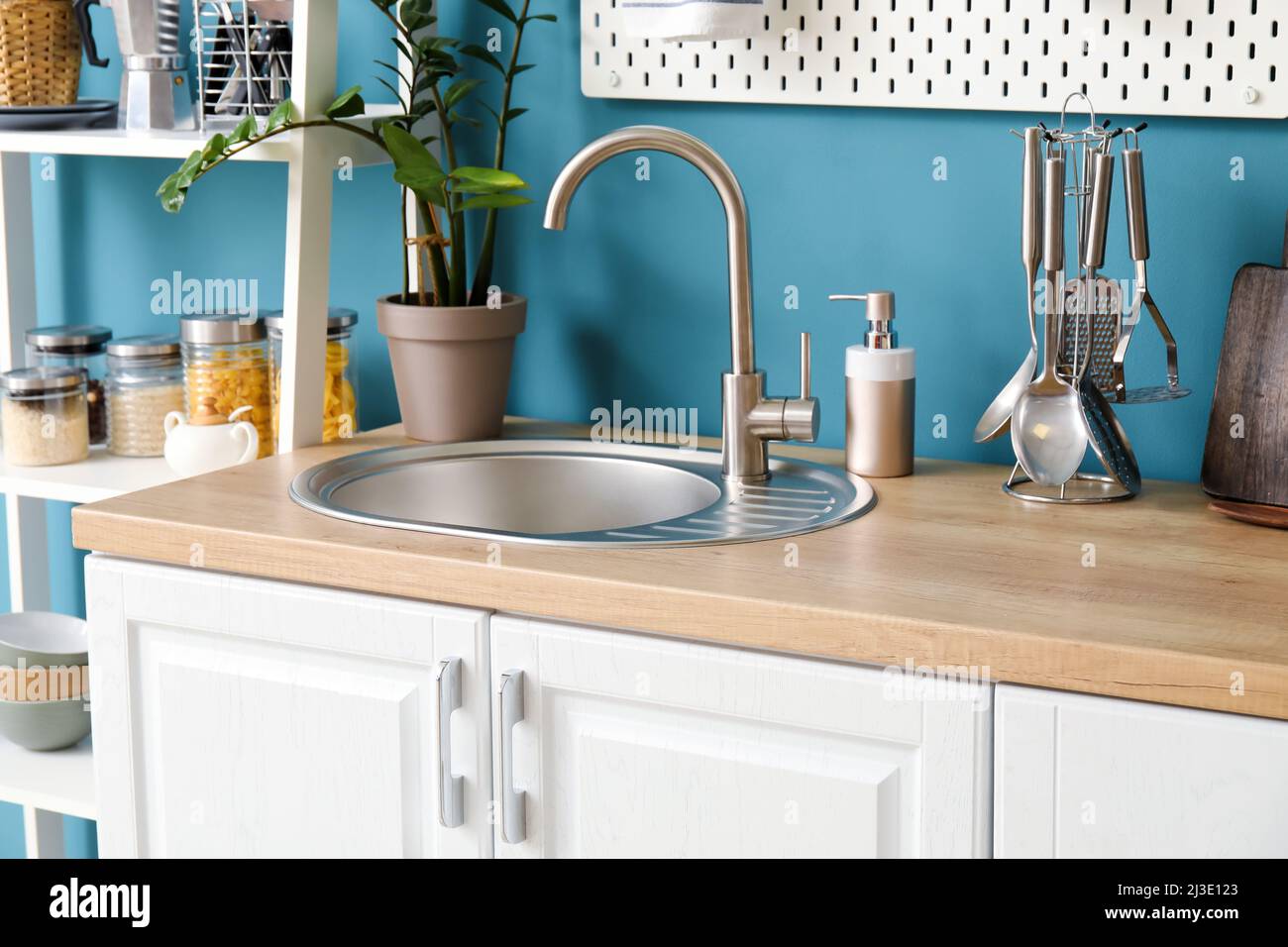 Comptoir en bois avec évier en argent, batterie de cuisine, lave-vaisselle  et savon près du mur bleu dans la cuisine Photo Stock - Alamy